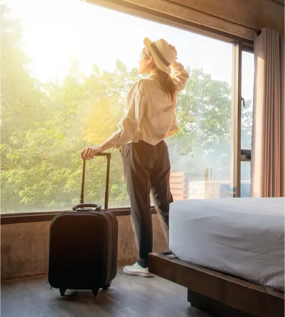 Person with suitcase looking out hotel window