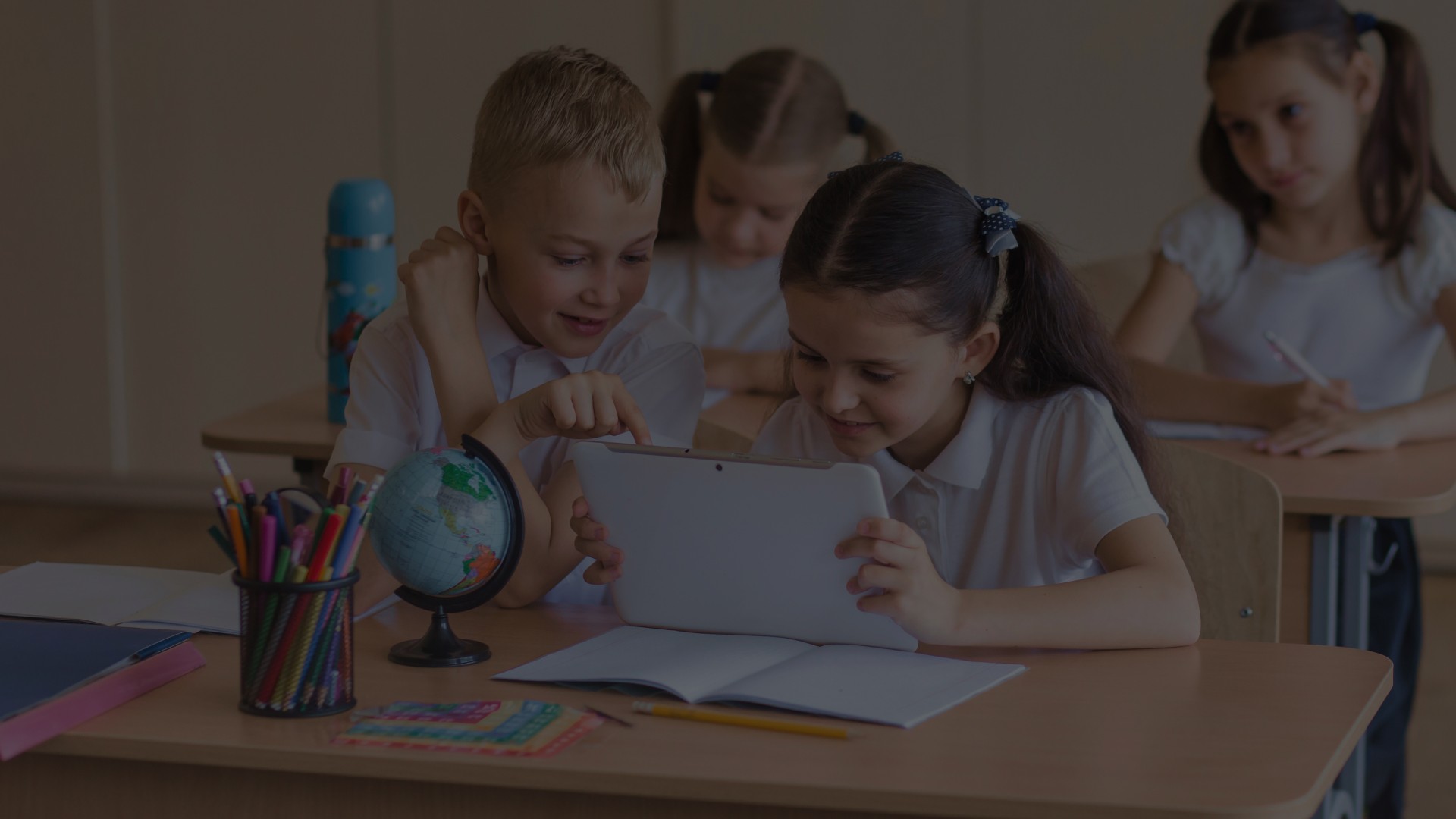 School Children Using a Tablet for Interactive Digital Learning in a Classroom