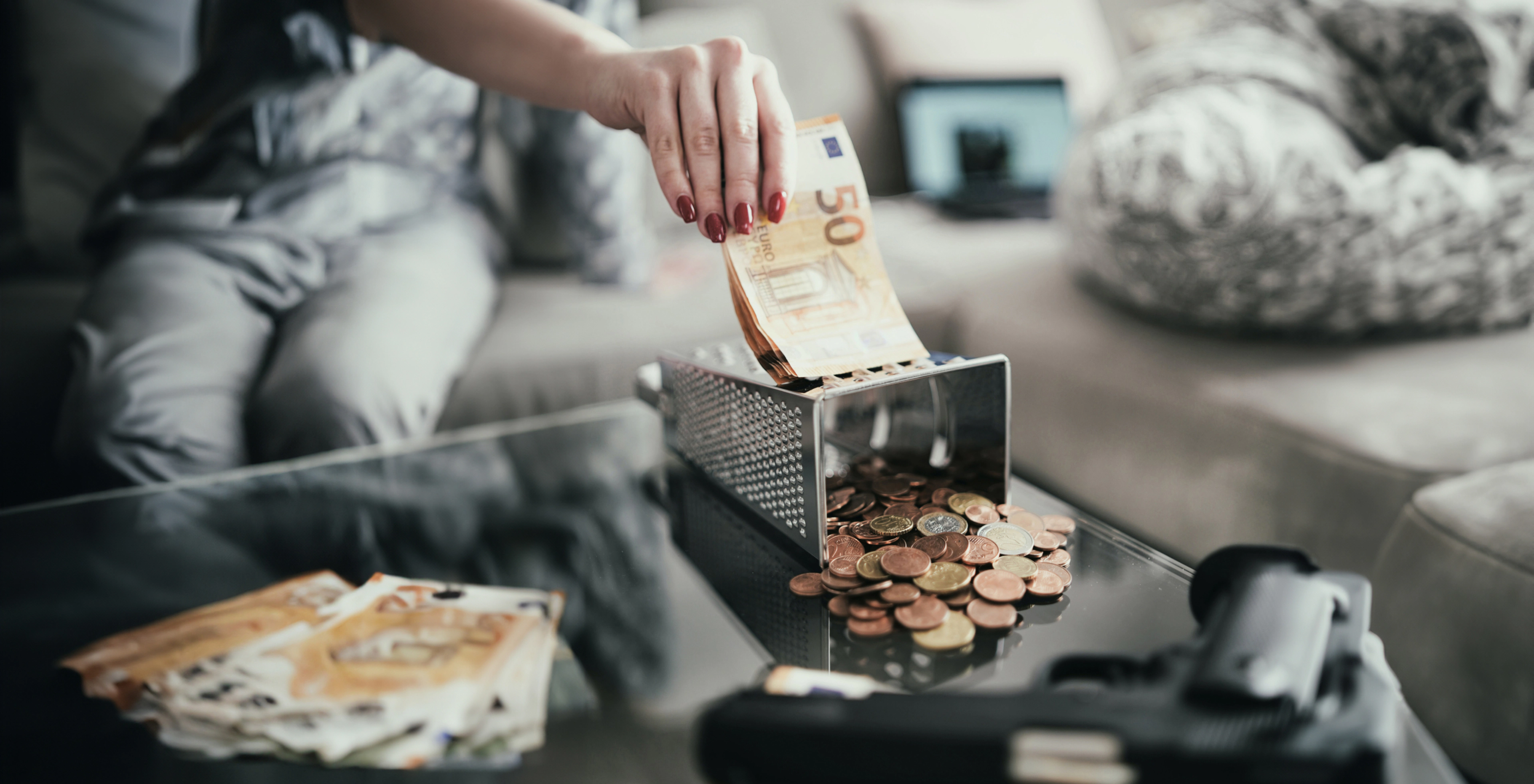 Hand putting euro bills on table with coins and handgun visible